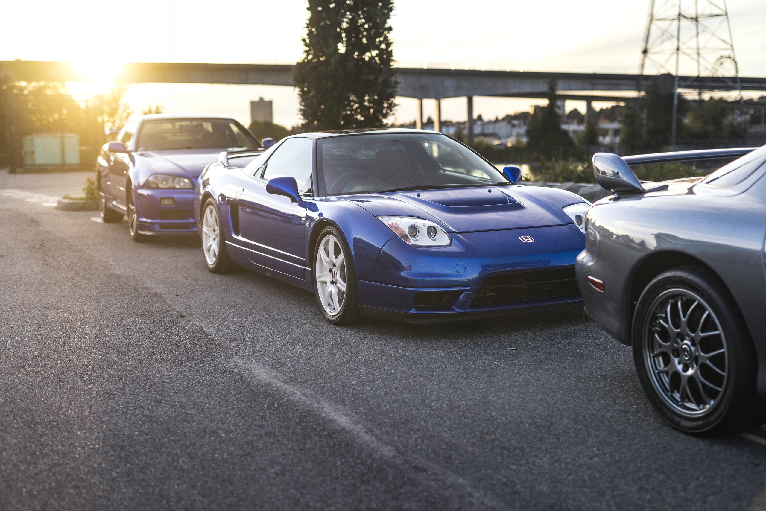 The blue NSX-R in three-quarter view between the other cars, backlit by the setting sun