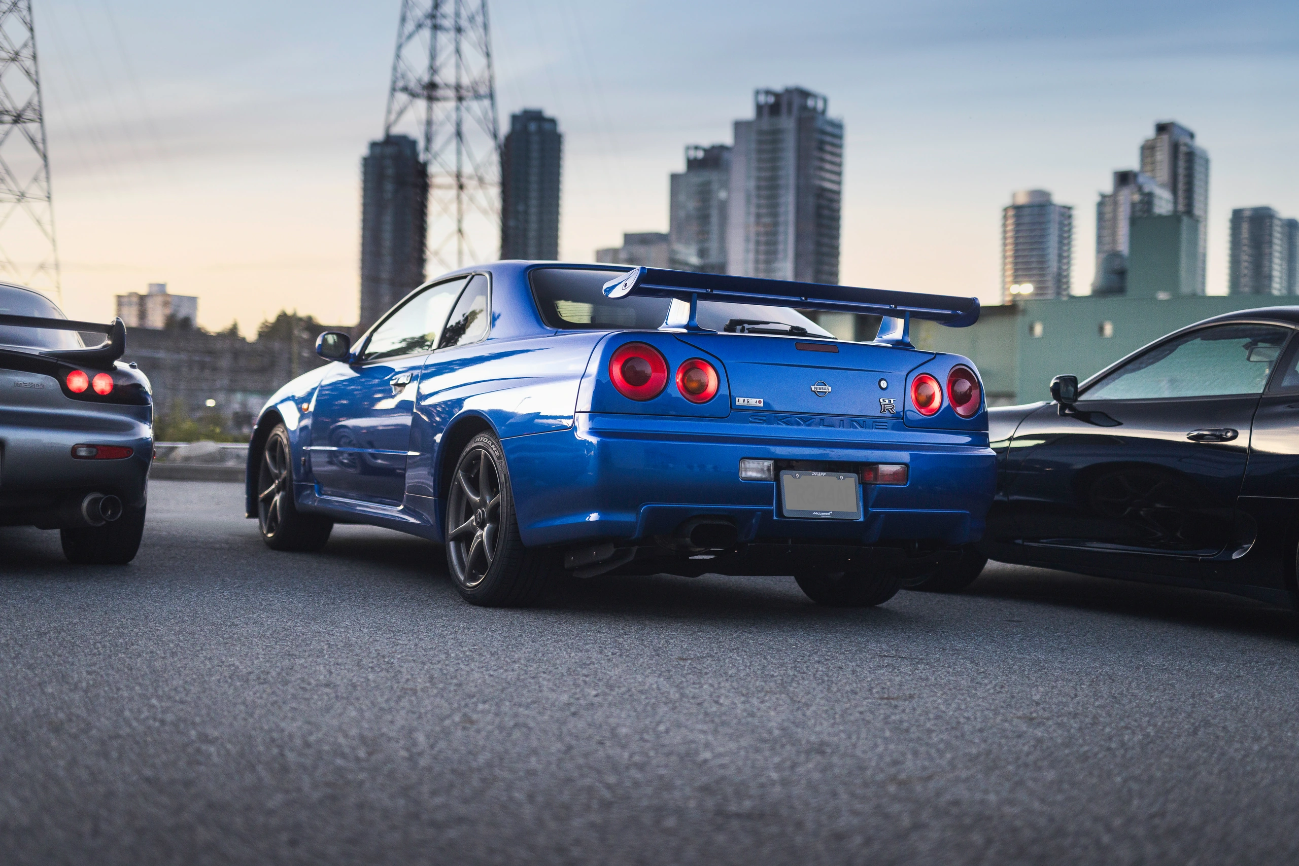 The R34 GT-R's four round tail lamps and rear wing against the city skyline