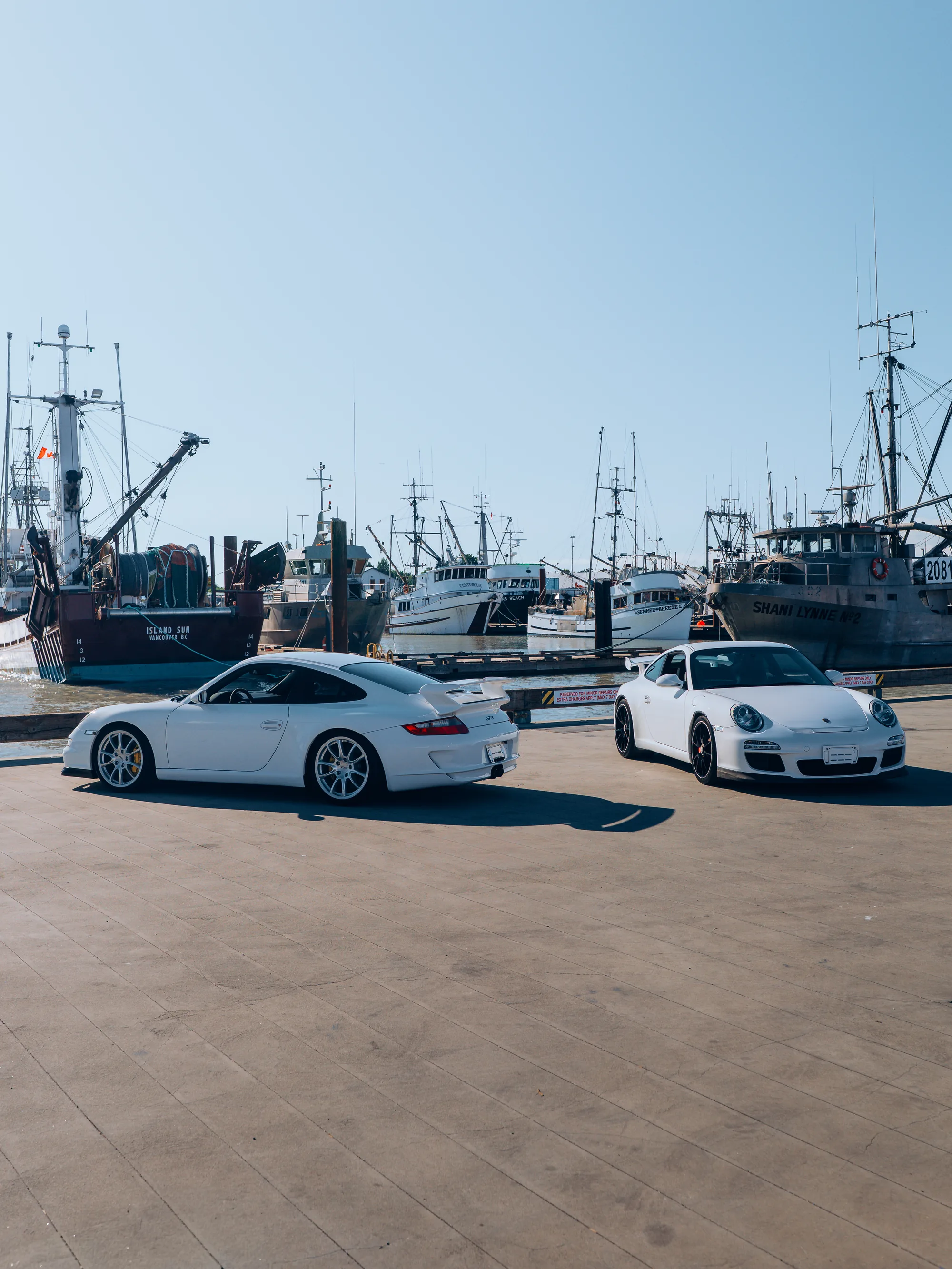 Two white Porsche 911 GT3s across a Japanese harbour apron